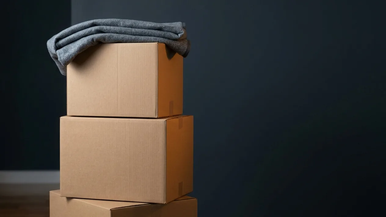 A stack of sealed moving cartons with a folded moving blanket resting on top